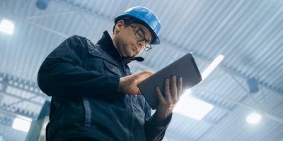 Factory worker in a hard hat is using a tablet computer.